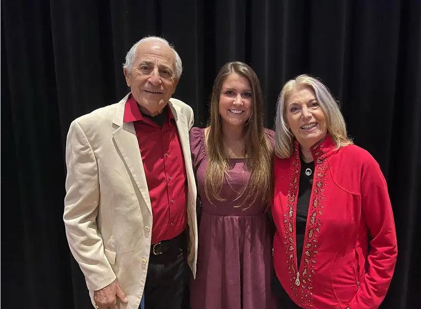 A man and two women are posing for a picture in front of a black curtain.