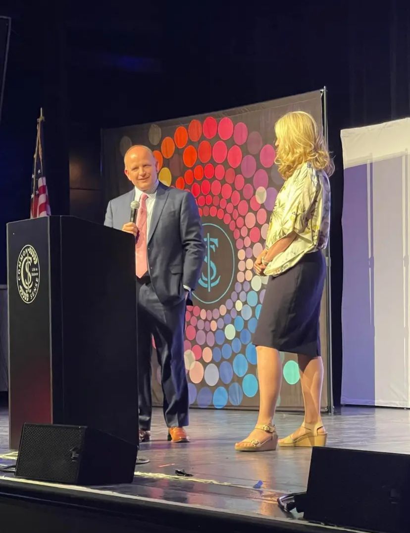 A man in a suit and tie is standing next to a woman on a stage.