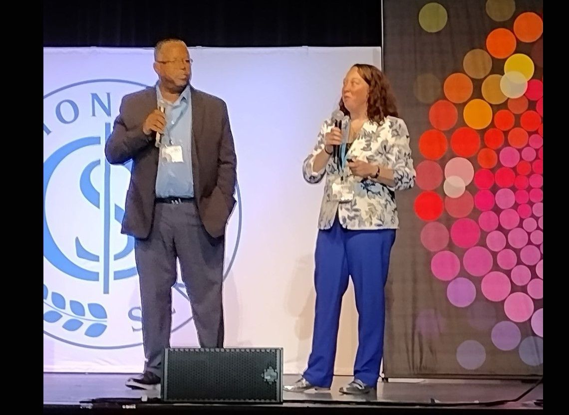 A man and a woman are standing on a stage talking into microphones
