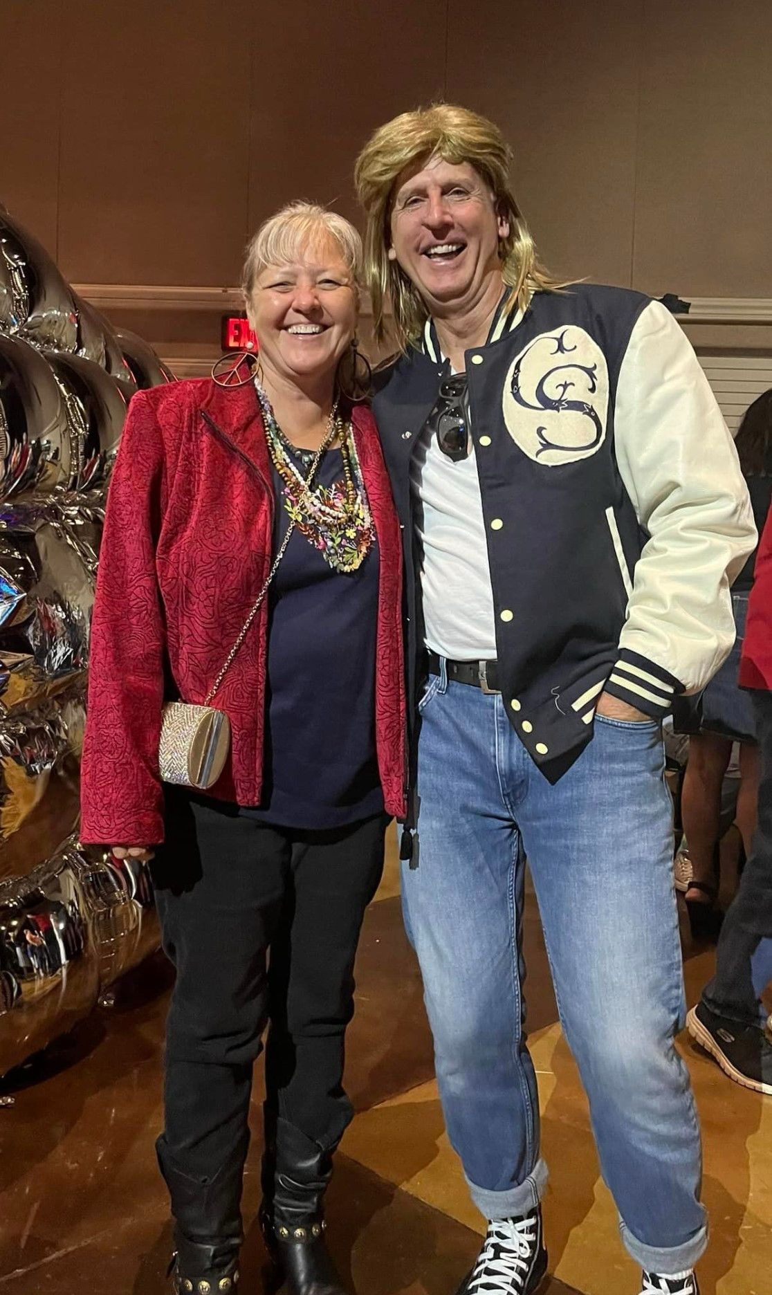 A man and a woman are posing for a picture together . the man is wearing a varsity jacket.