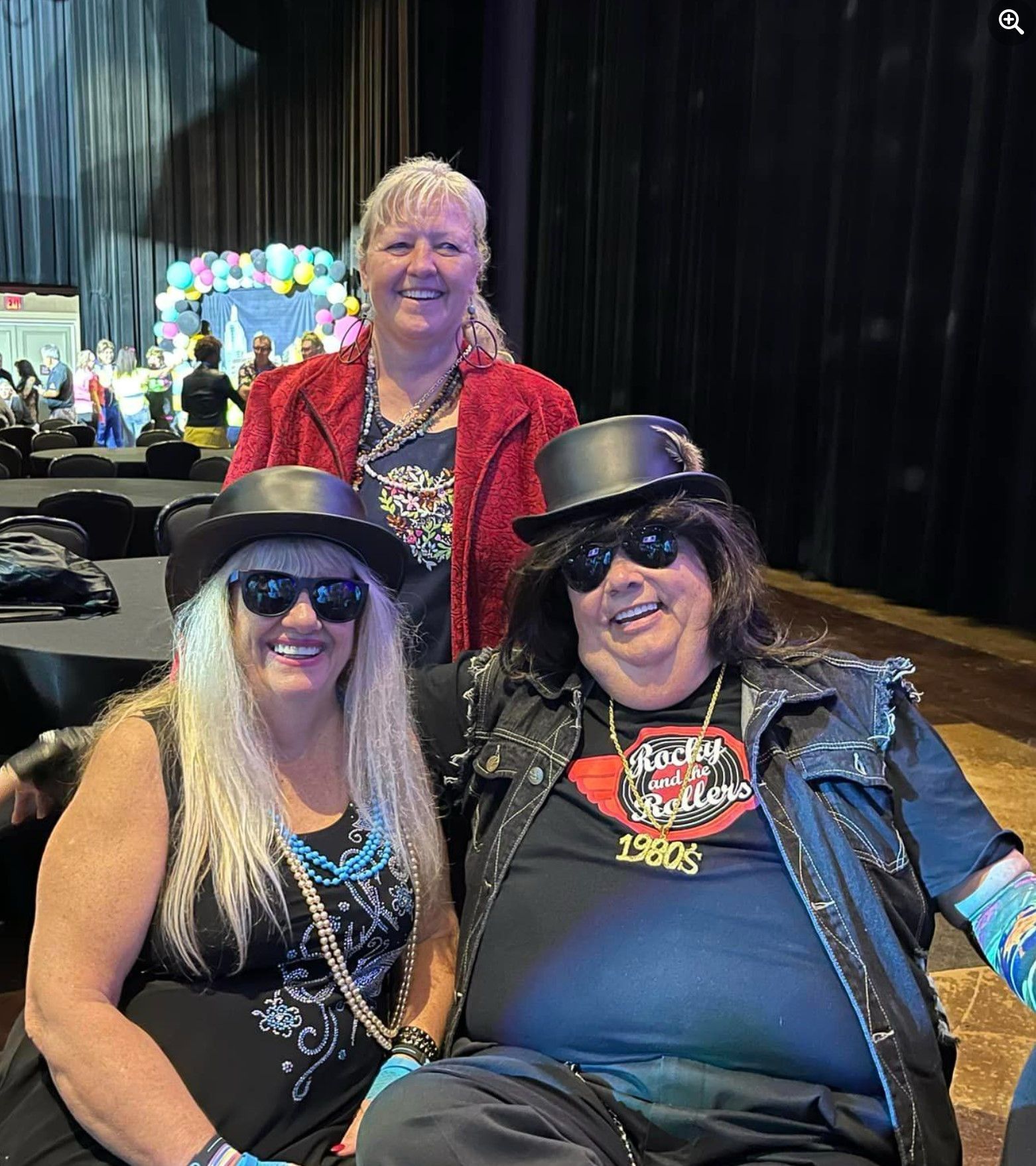 Three women are posing for a picture in front of a stage.
