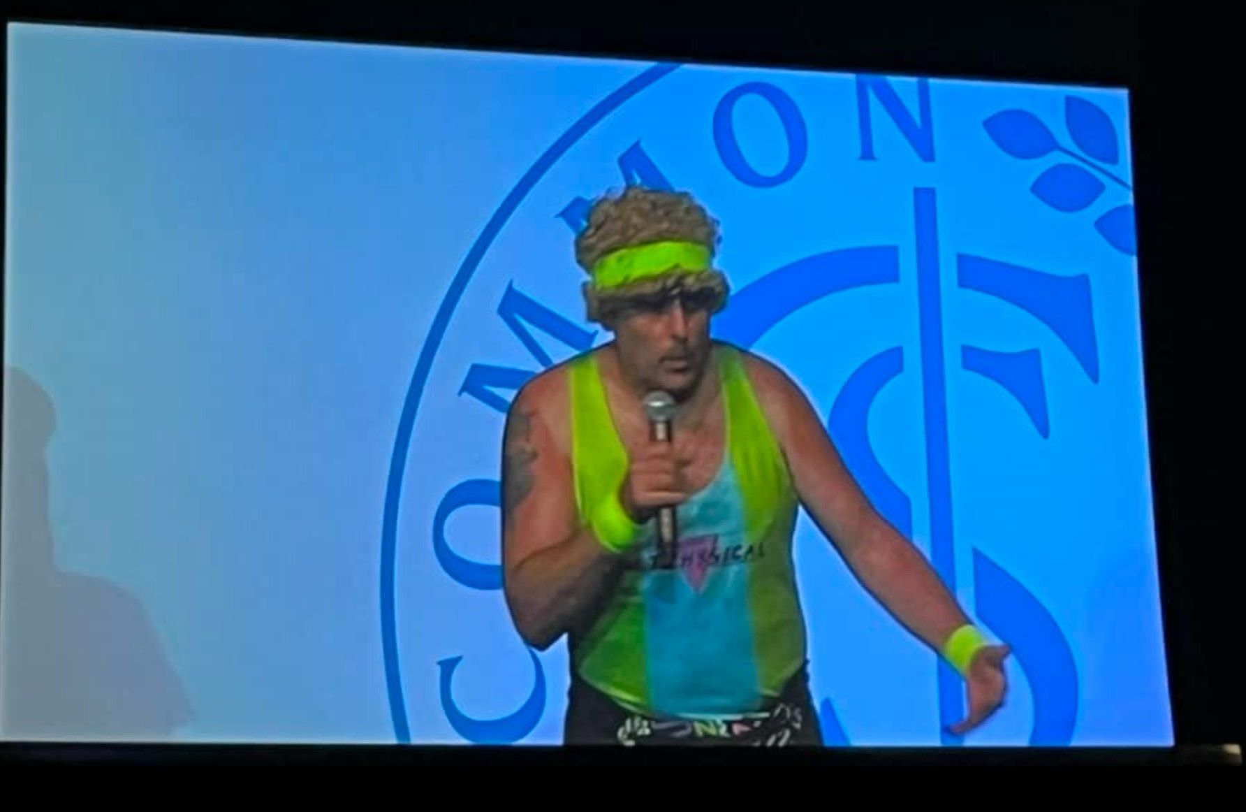 A man is standing in front of a screen with the word common on it