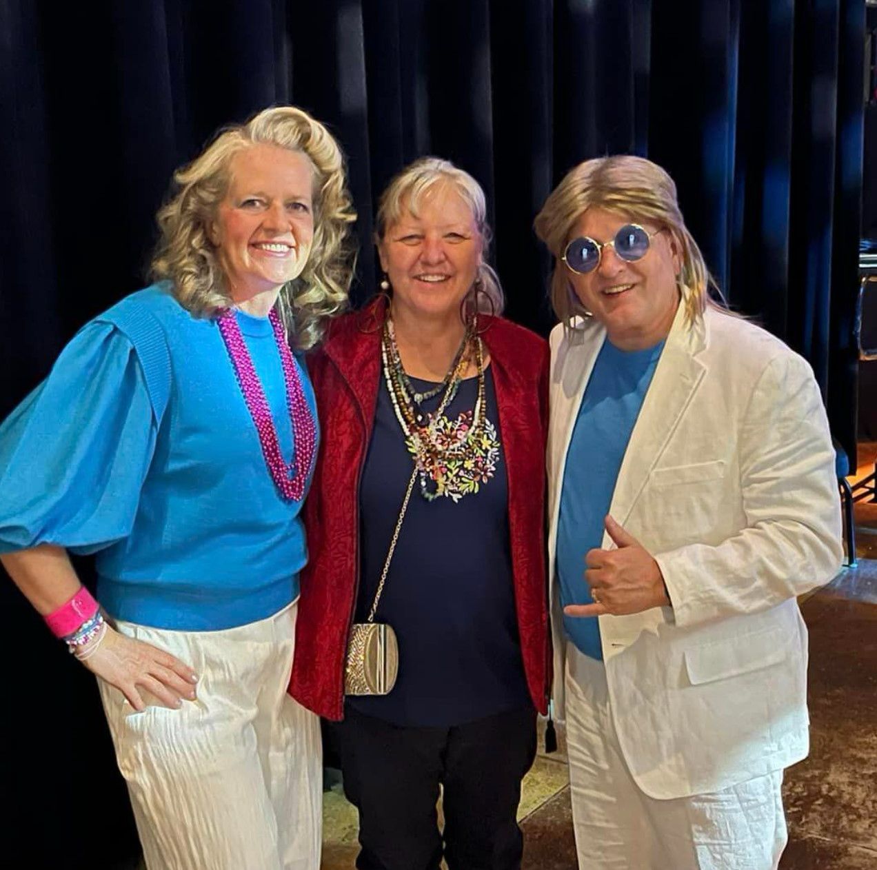 Three women and a man are posing for a picture in front of a black curtain.