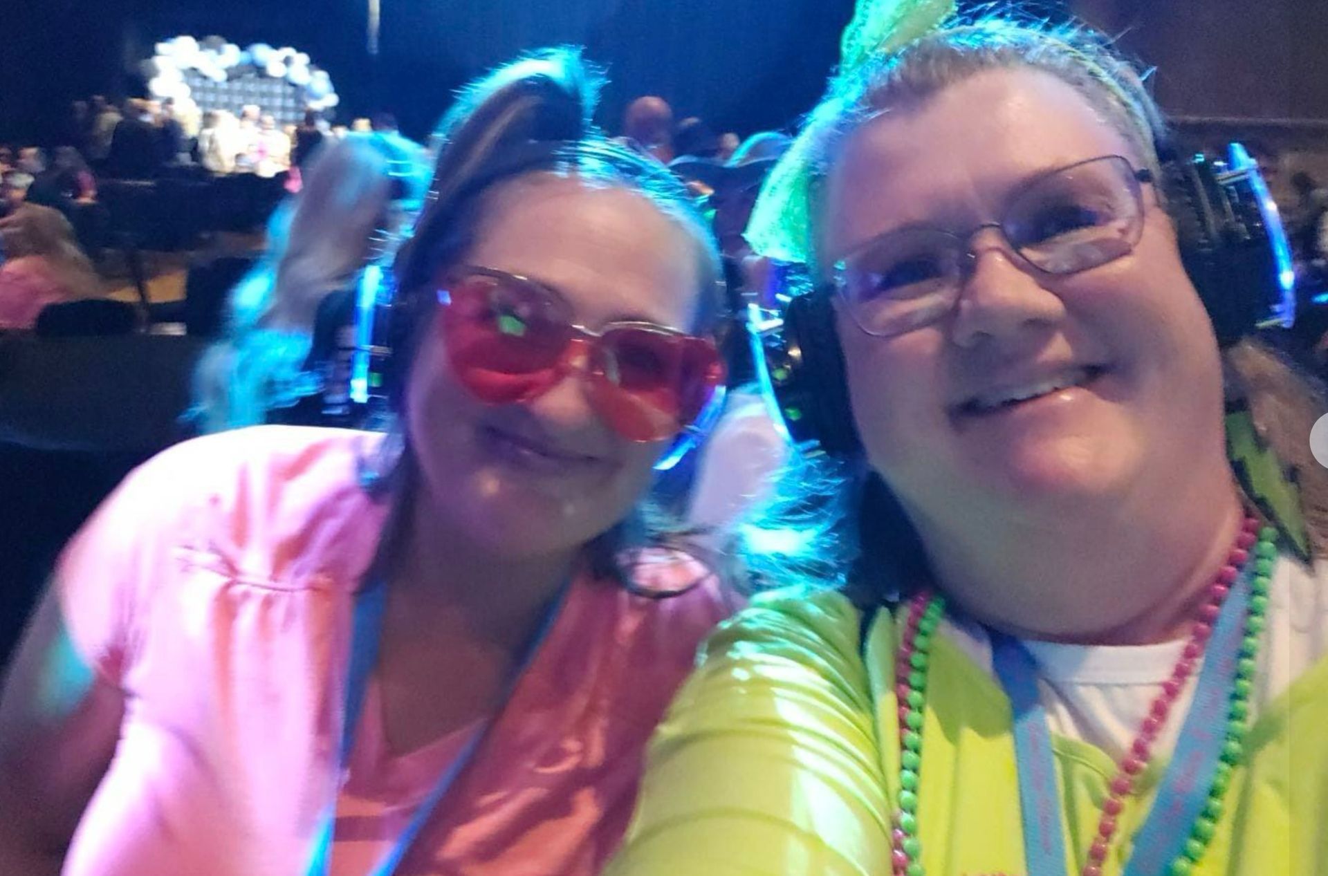 Two women wearing headphones and sunglasses are posing for a selfie.