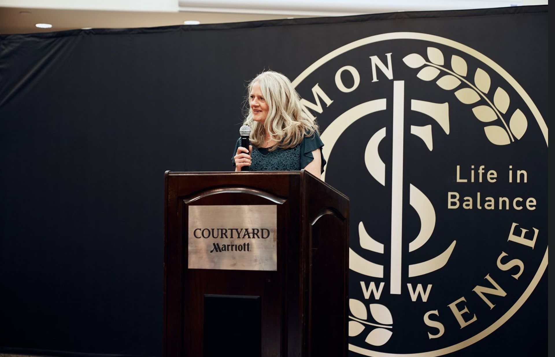 A woman is standing at a podium holding a microphone.