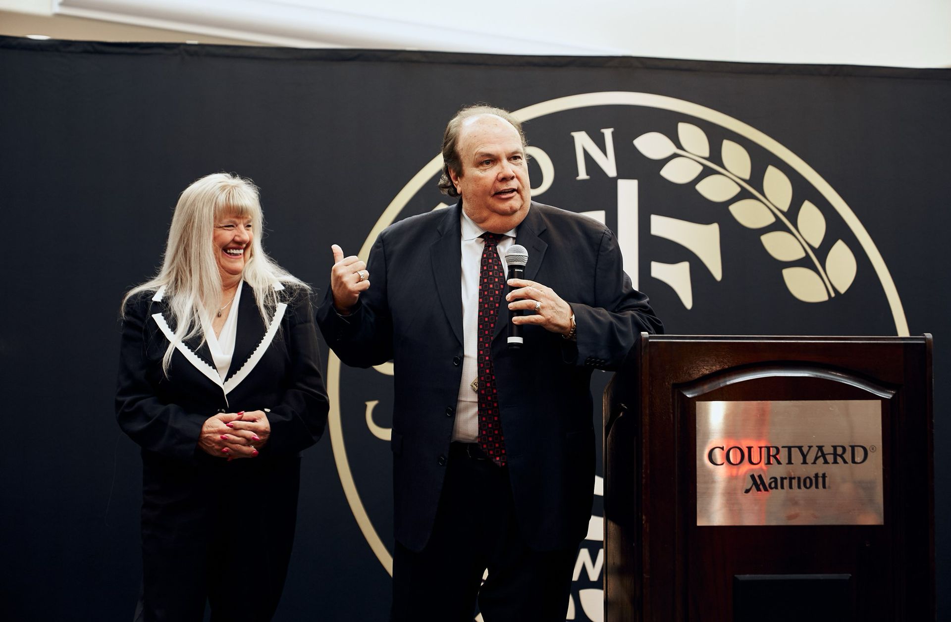 A man is standing at a podium holding a microphone next to a woman.