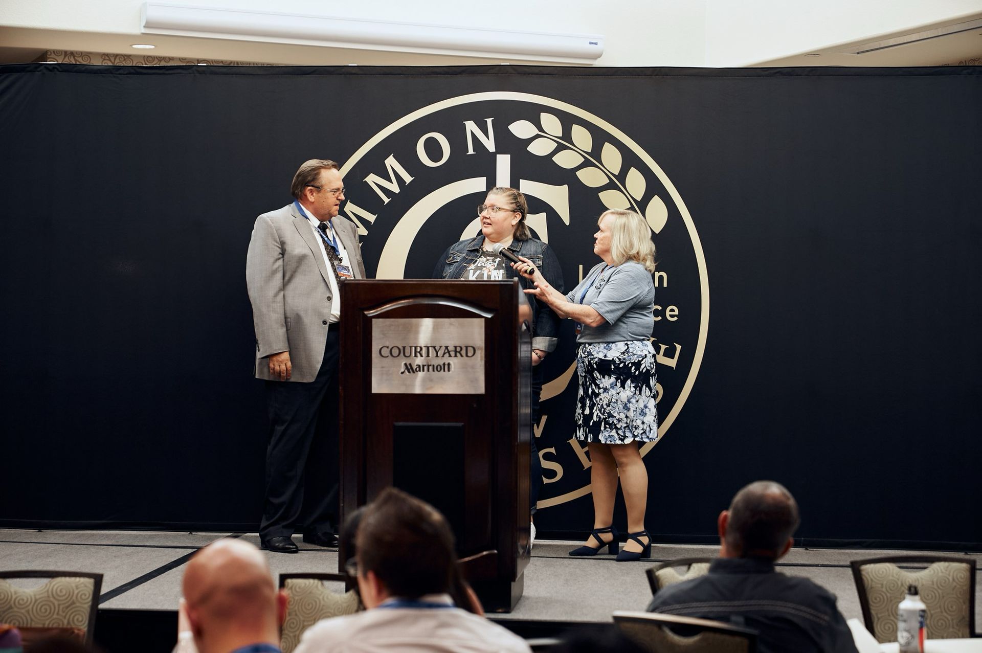 Two men and a woman are standing at a podium in front of a crowd.