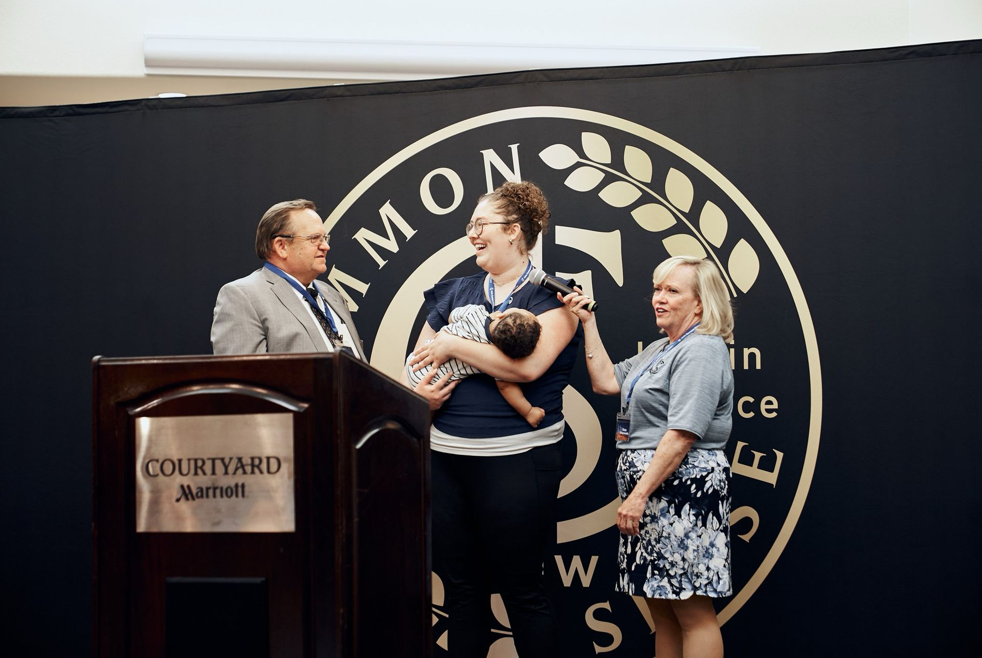 A woman is holding a baby in front of a courtyard marriott logo.