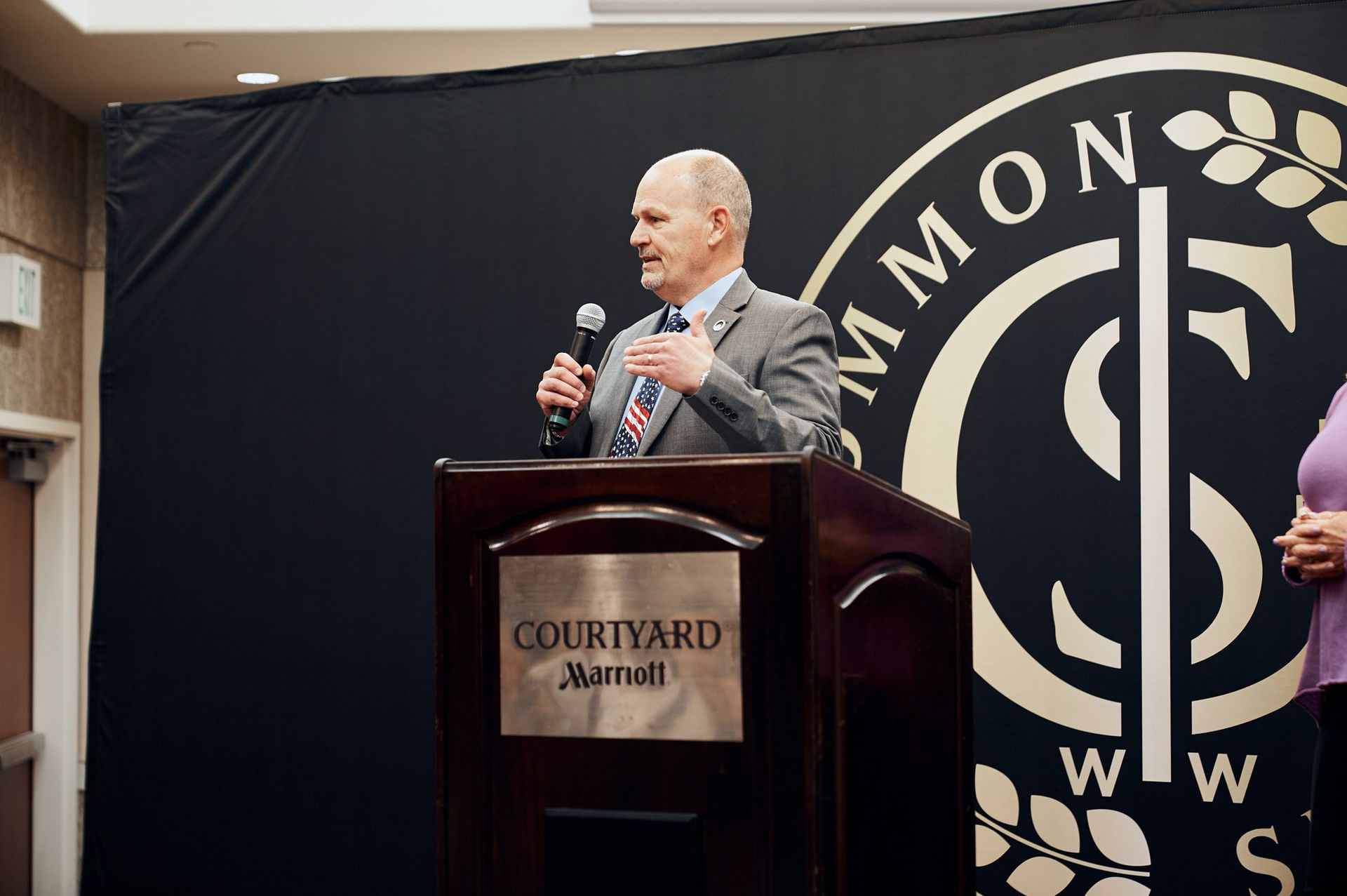 A man in a suit and tie is standing at a podium holding a microphone.