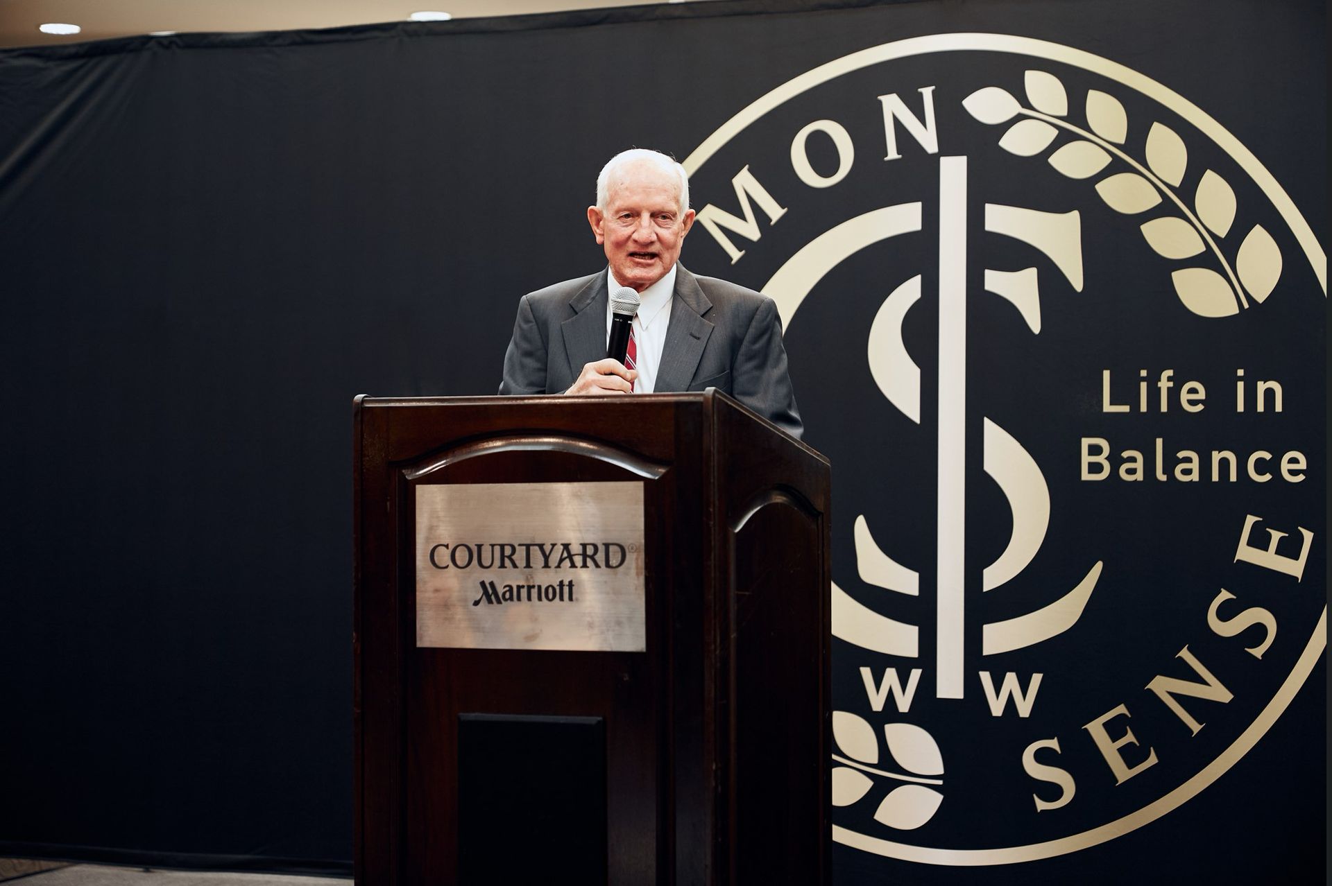 A man is standing at a podium in front of a sign that says life in balance