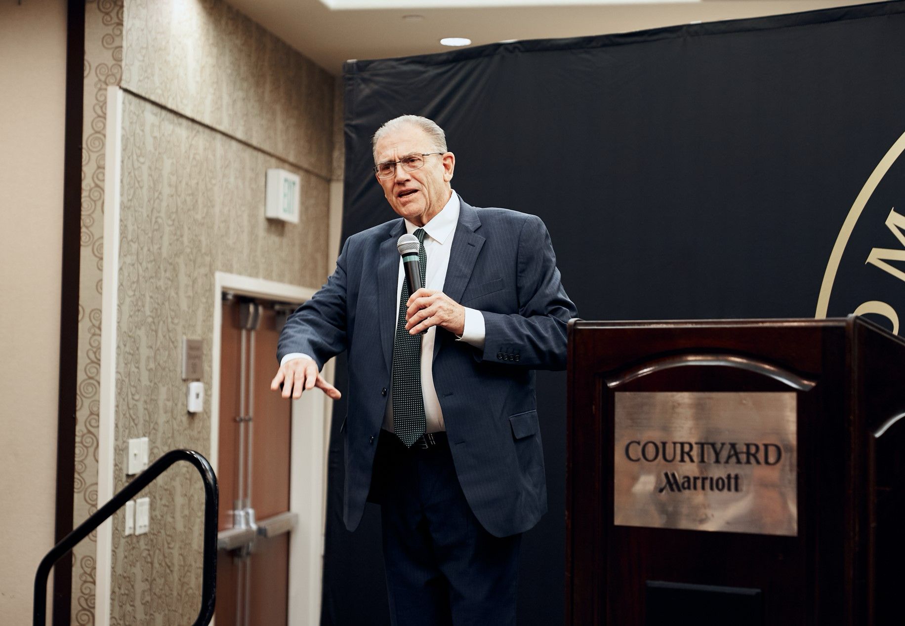 A man in a suit and tie is standing at a podium holding a microphone.