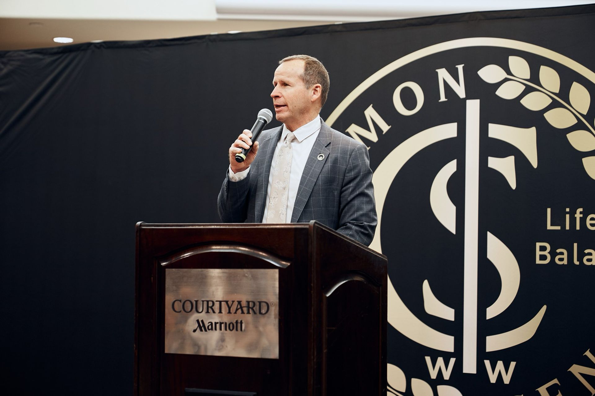 A man stands at a podium holding a microphone in front of a sign that says courtyard marriott