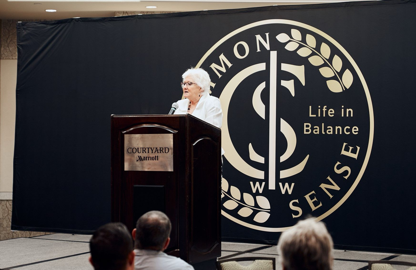 A woman stands at a podium in front of a sign that says life in balance