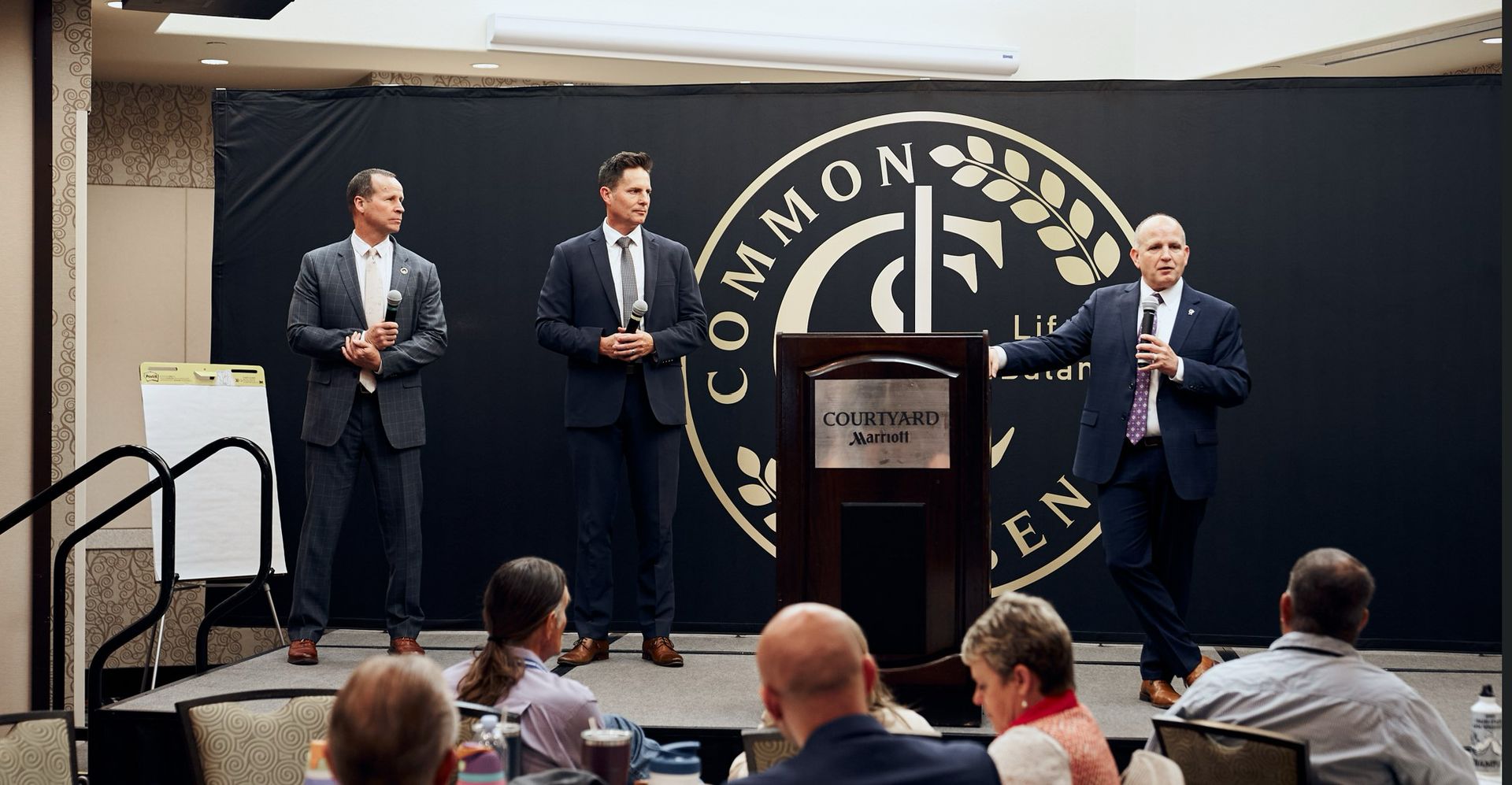 A group of men are standing on a stage giving a presentation to a group of people.