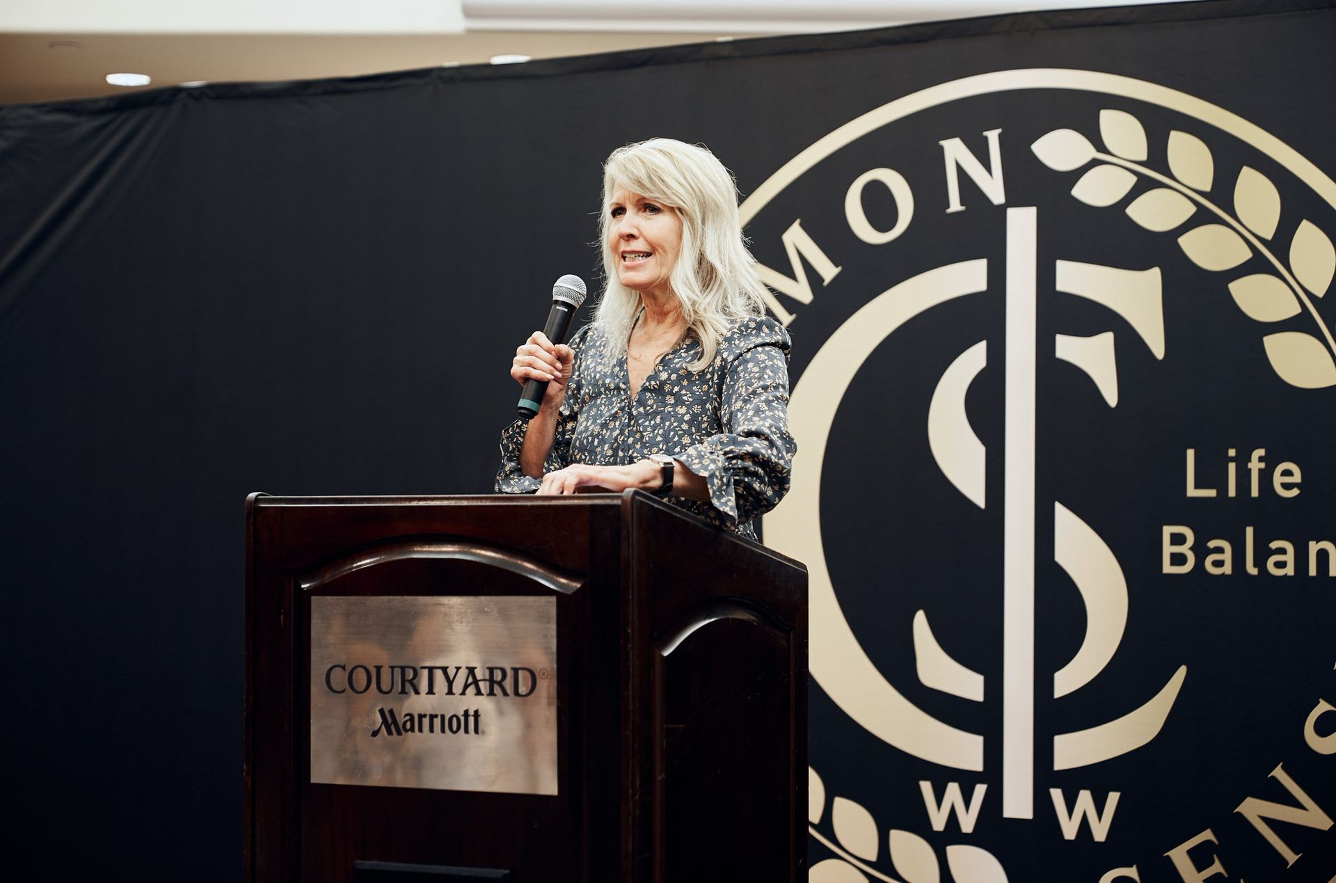 A woman is standing at a podium speaking into a microphone.