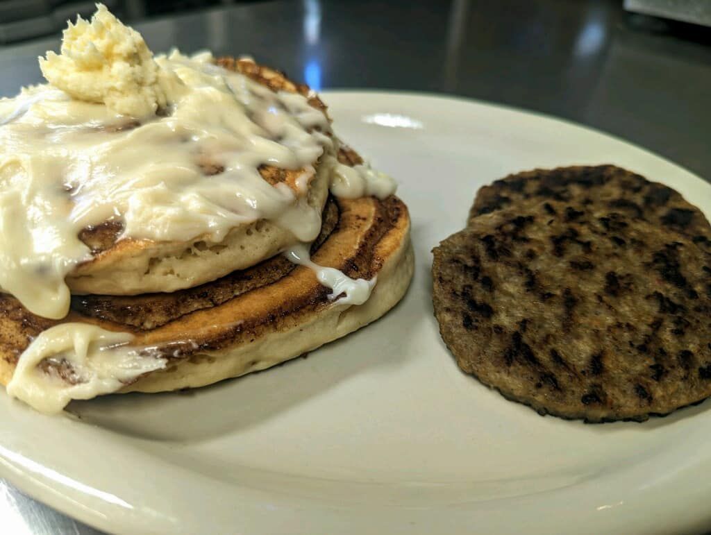 A white plate topped with a stack of cinnamon rolls and a sausage patty.