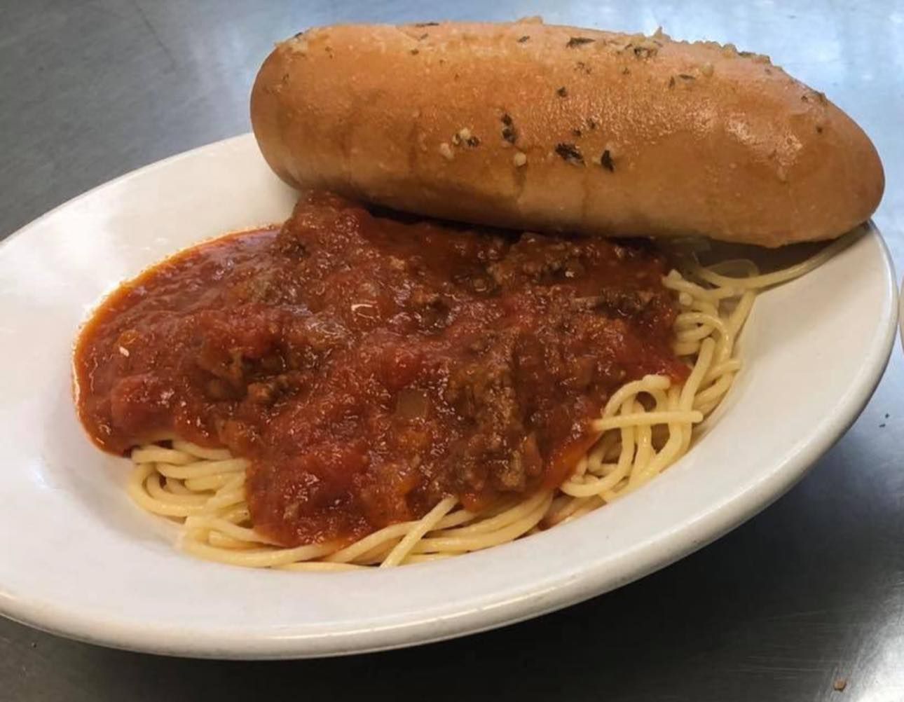 A white plate topped with spaghetti and meat sauce and a garlic bread roll.