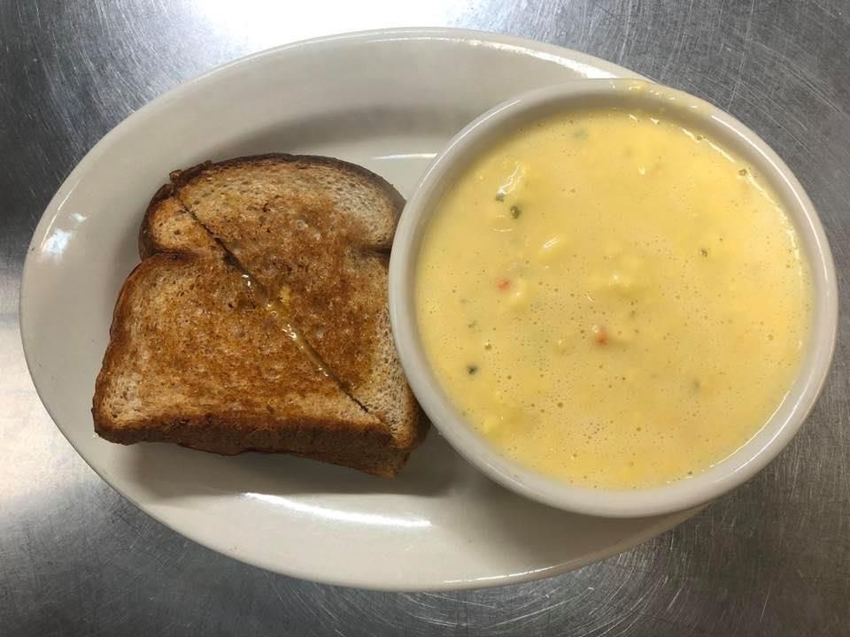 A plate of food with a bowl of soup and a piece of grilled cheese.