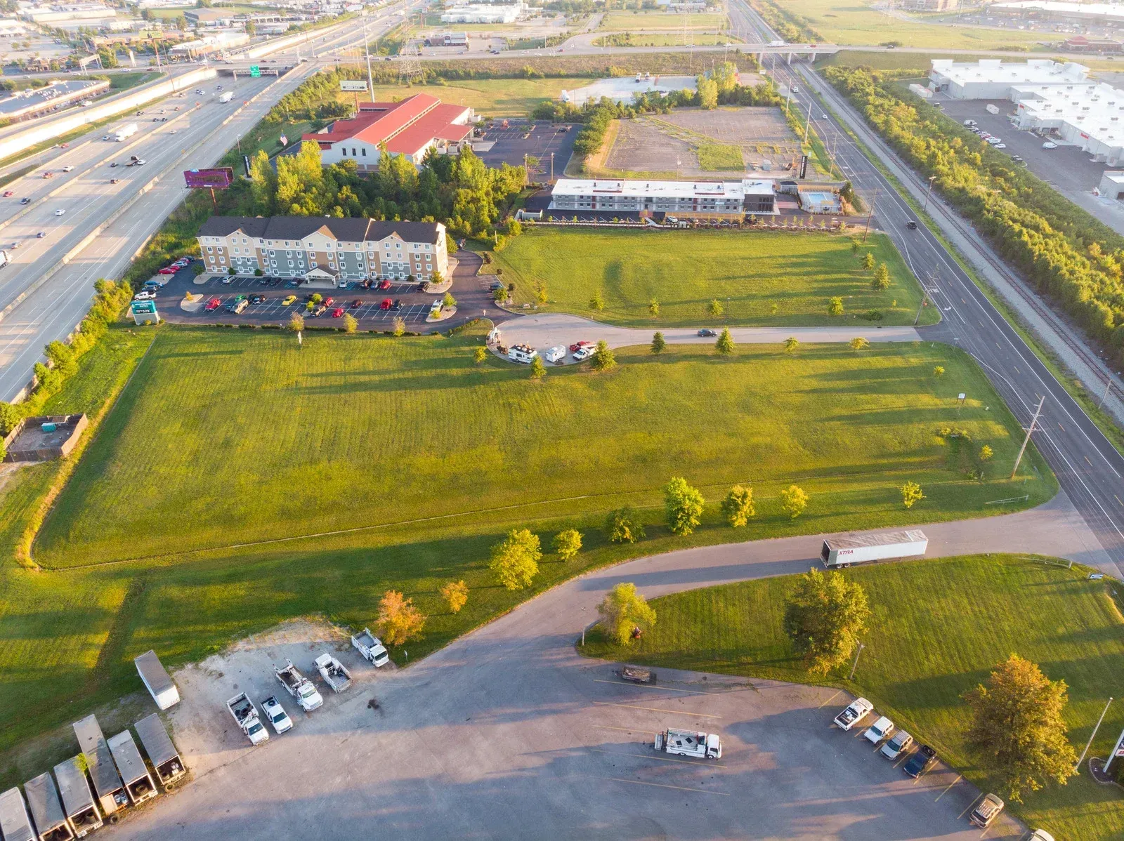 Aerial view of a green field with marked plots, surrounded by houses under a blue sky.