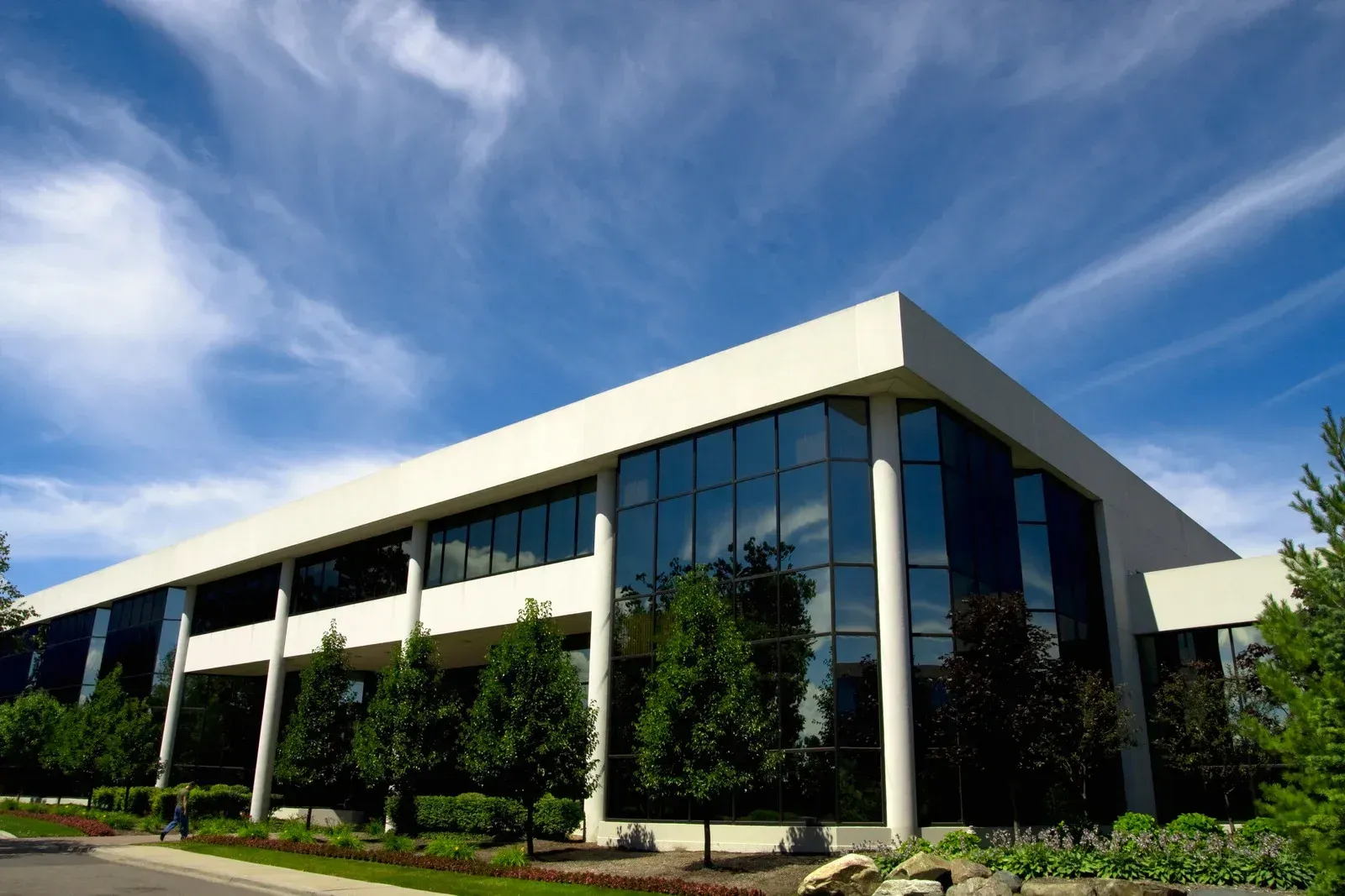 Modern, two-story office building with glass windows, white trim, and a bright blue sky.