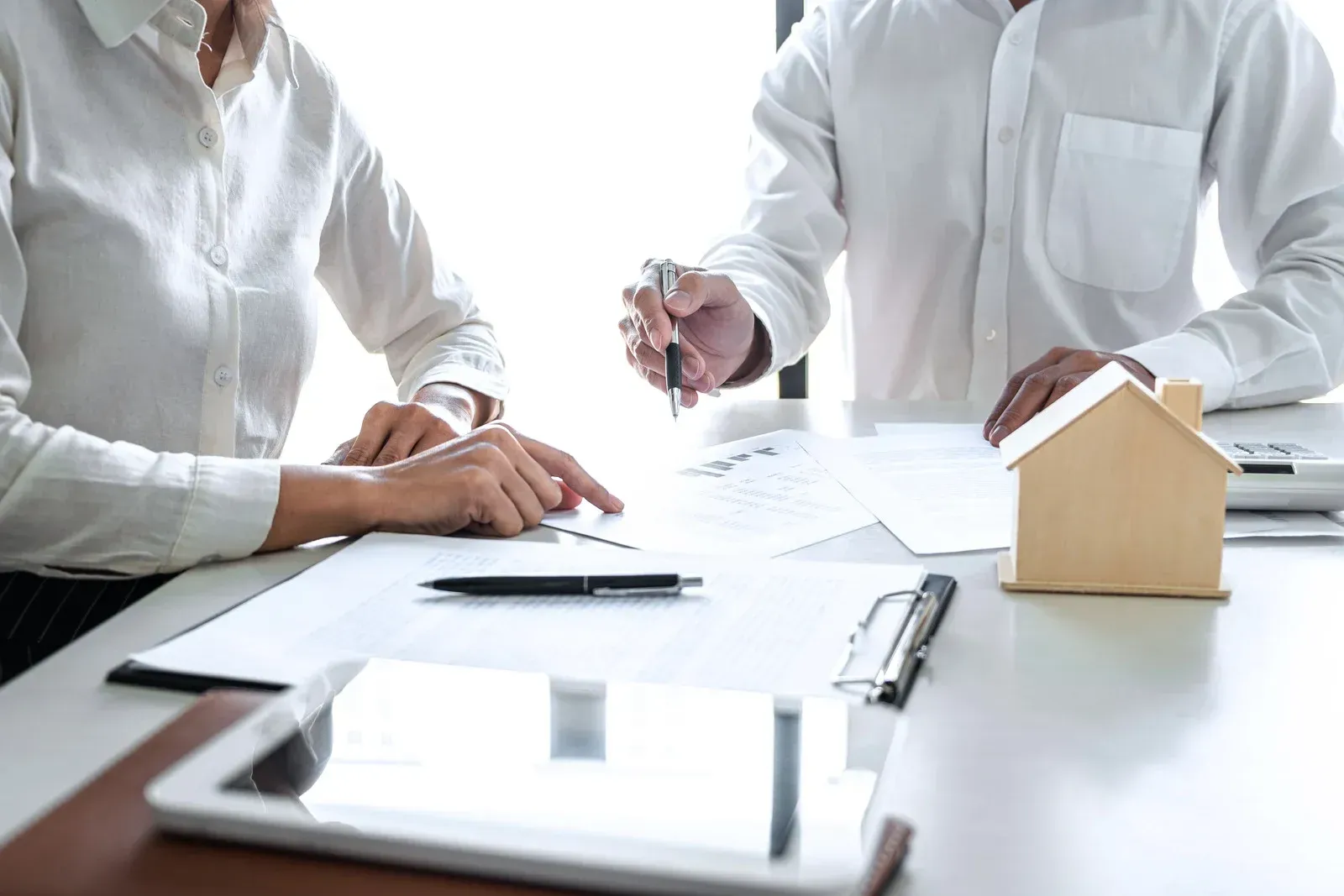 Two people reviewing documents at a table; a small house model sits nearby.