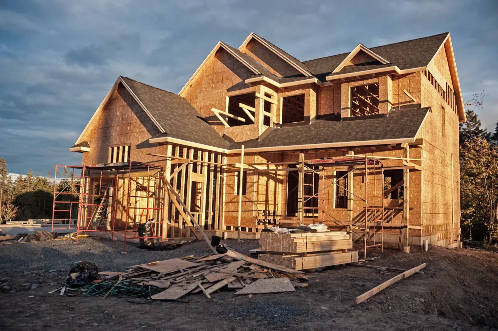House under construction, wooden frame, unfinished windows, and materials scattered in front.