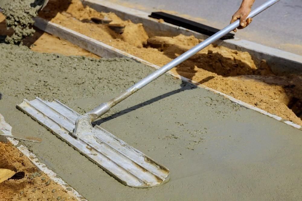 a person is using a trowel to spread concrete on the ground .