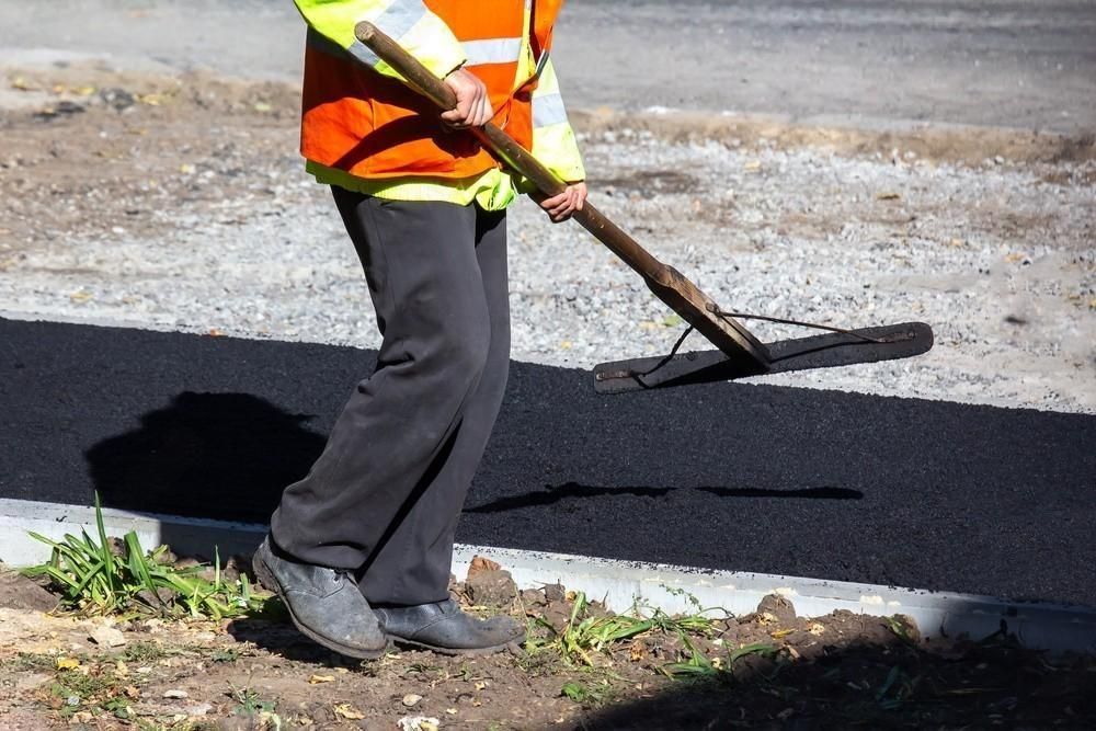a man is using a rake to spread asphalt on a road .