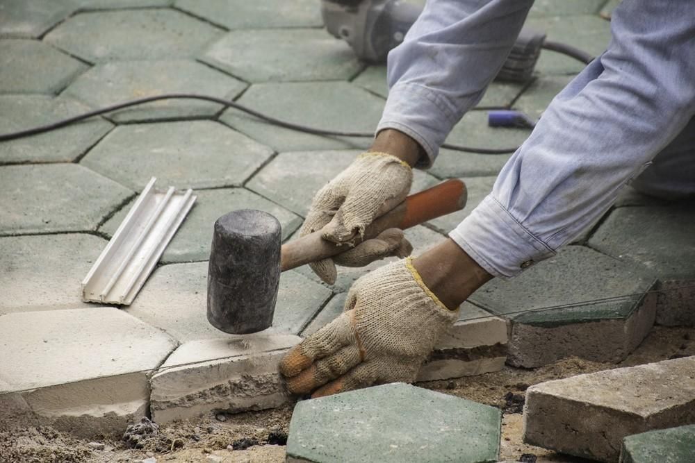 a man is using a hammer to hammer bricks on a sidewalk .
