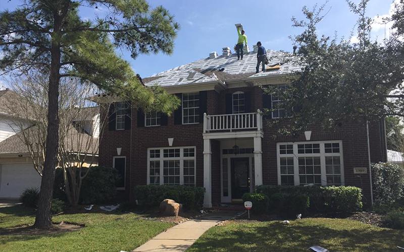 Two men are working on the roof of a large brick house.