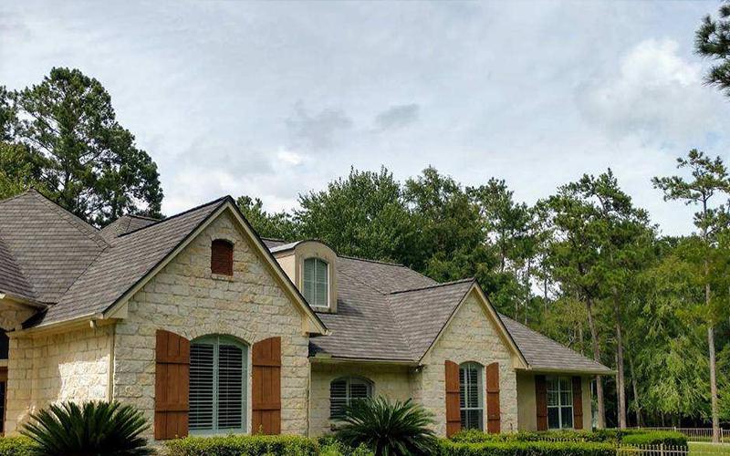 A large brick house with brown shutters is surrounded by trees