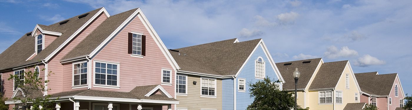 A row of colorful, suburban-style homes with gabled roofs under a blue sky.