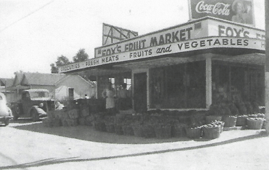 Foy's Fruit Market, old black and white photo. Storefront, baskets of produce, Coca-Cola sign.