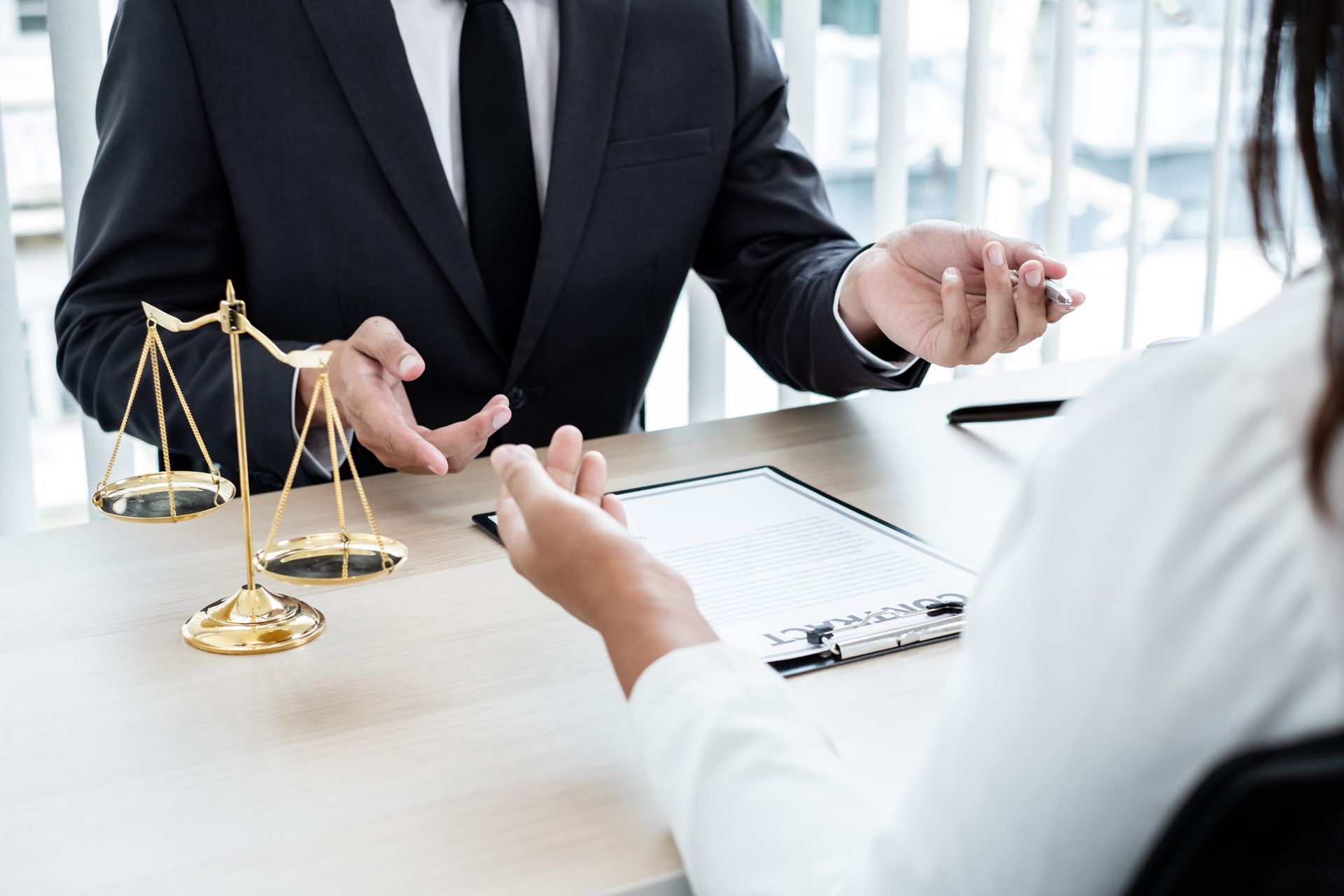 Lawyer consulting with a client across a desk beside gold balance scales