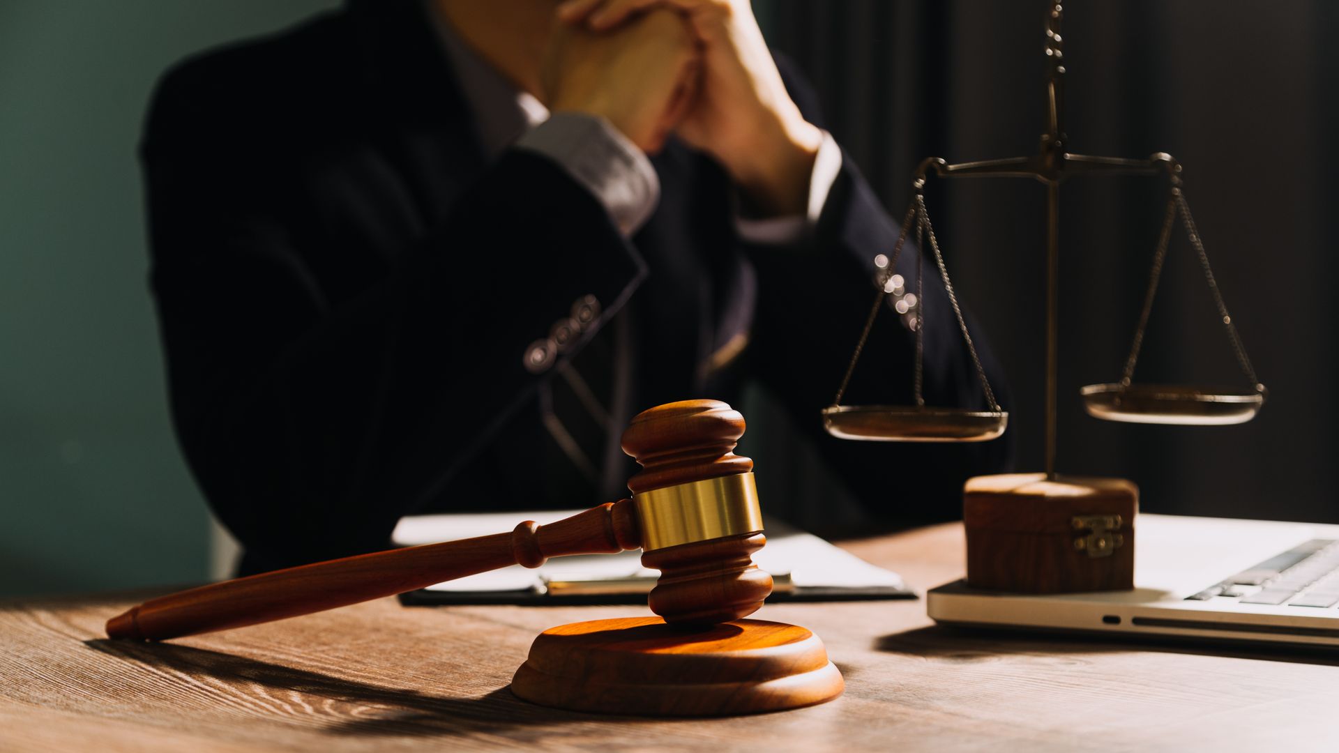 Judge at desk with gavel, scales of justice, and laptop.