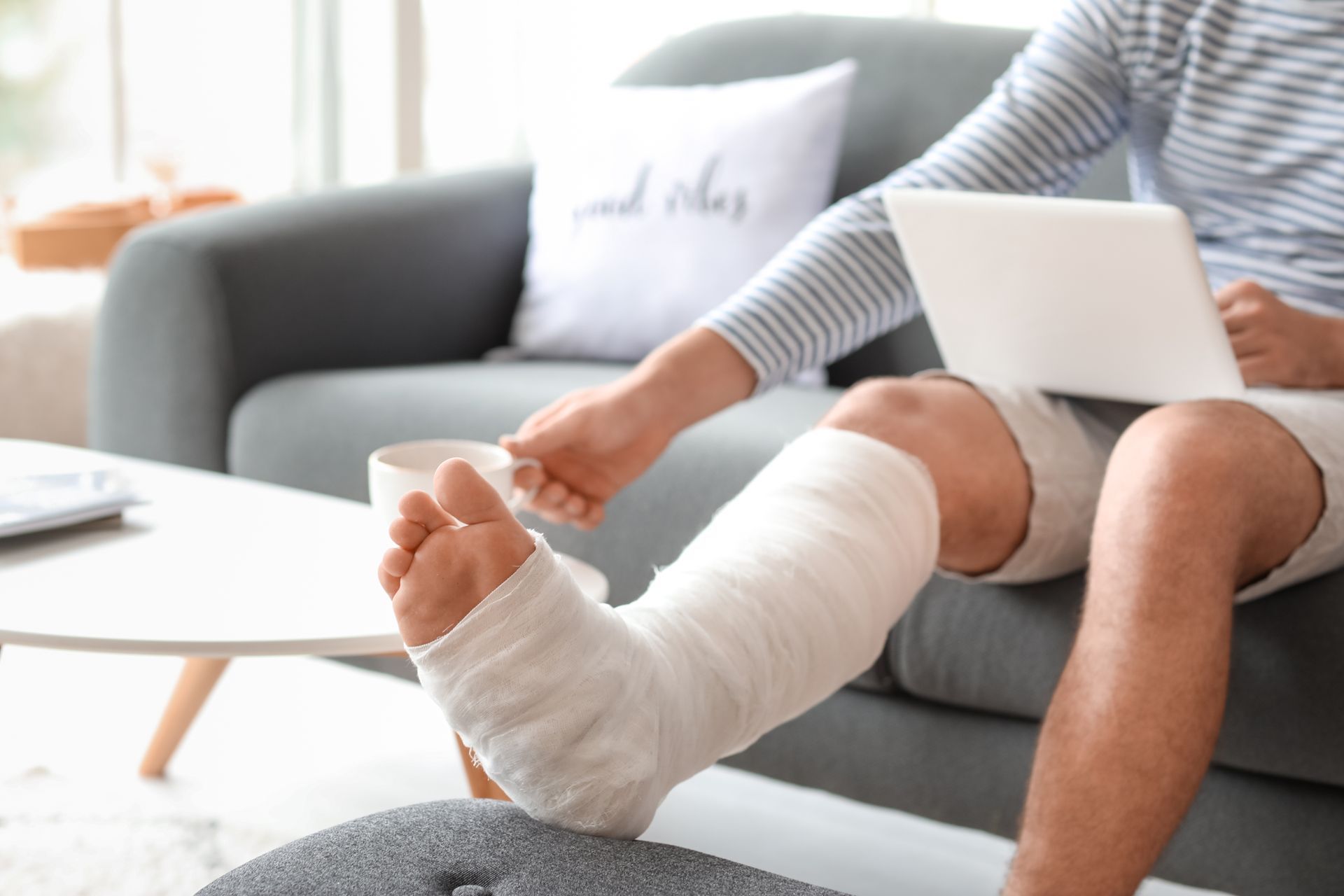 Man with leg cast works on a laptop while sitting on a couch, representing personal injury law.