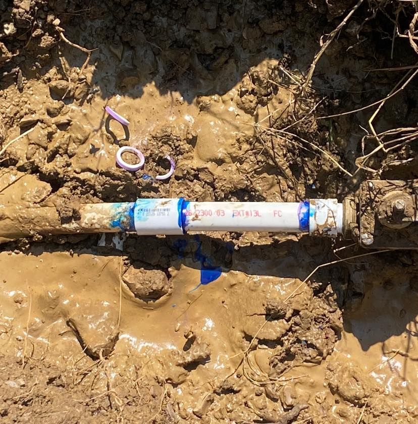 A white pipe is laying in the mud with a blue stripe on it