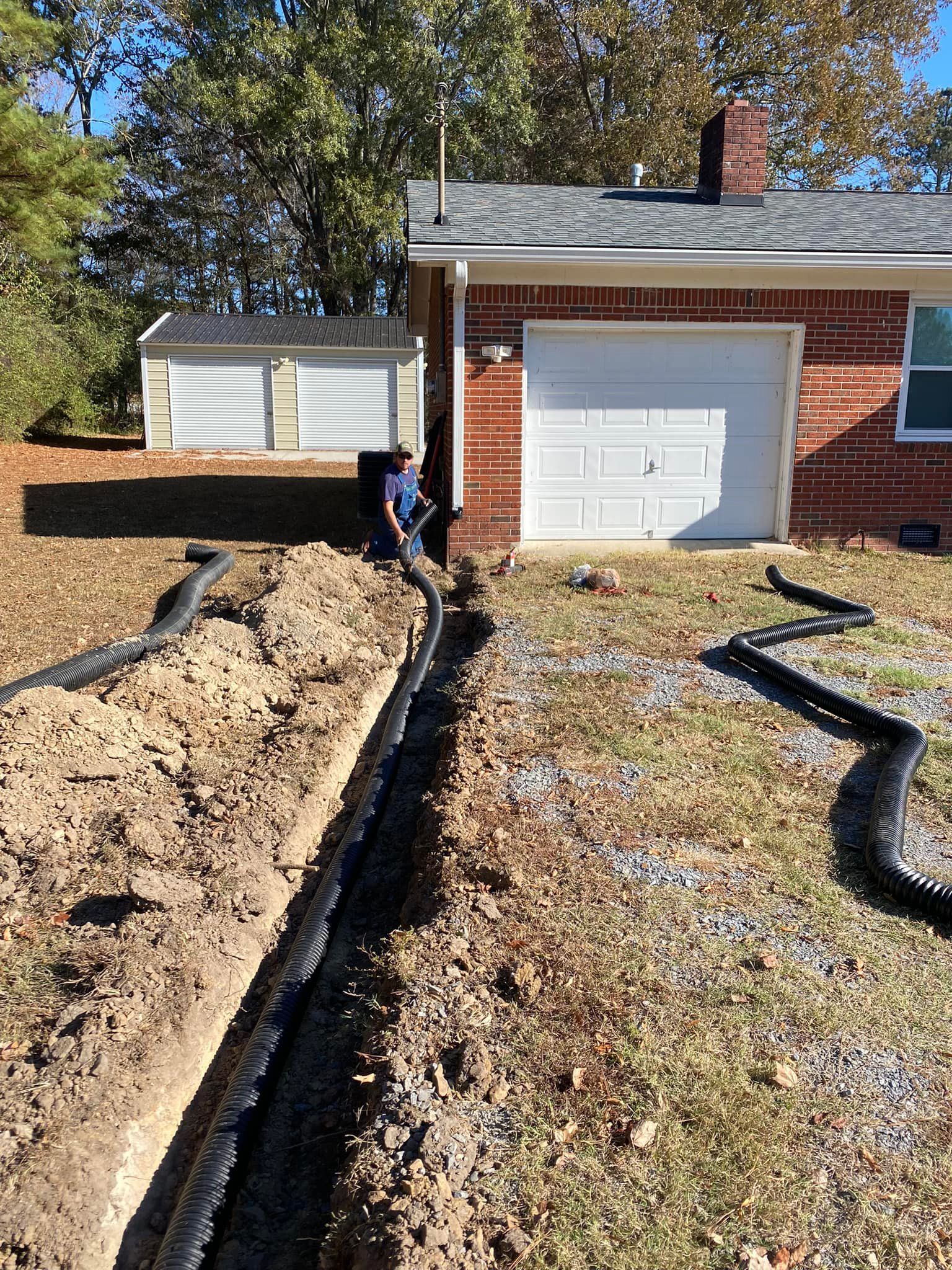 A man is digging a trench in front of a brick house.