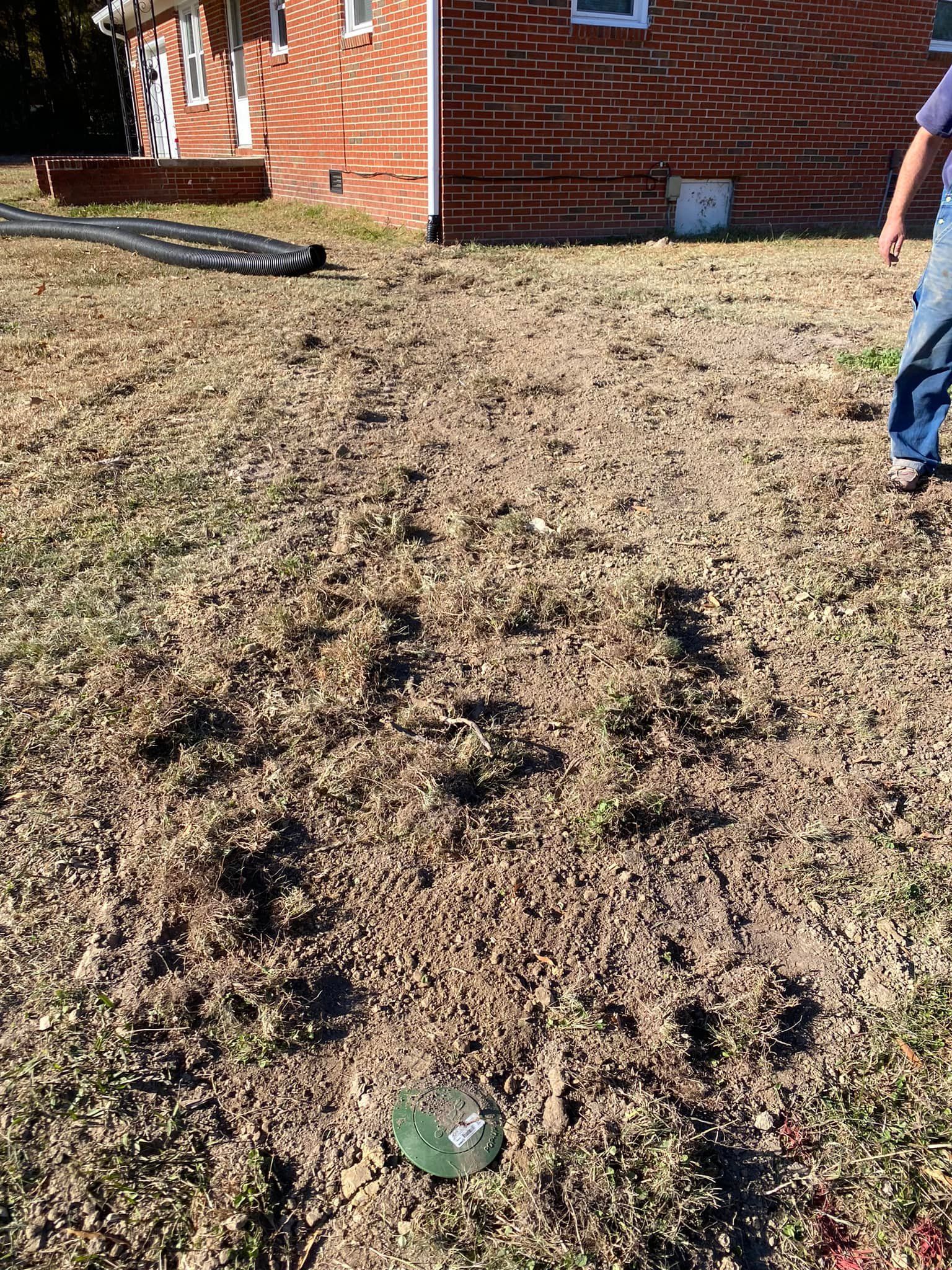 A man is standing in the dirt in front of a brick house.