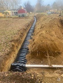 A black pipe is being installed in a trench of dirt.