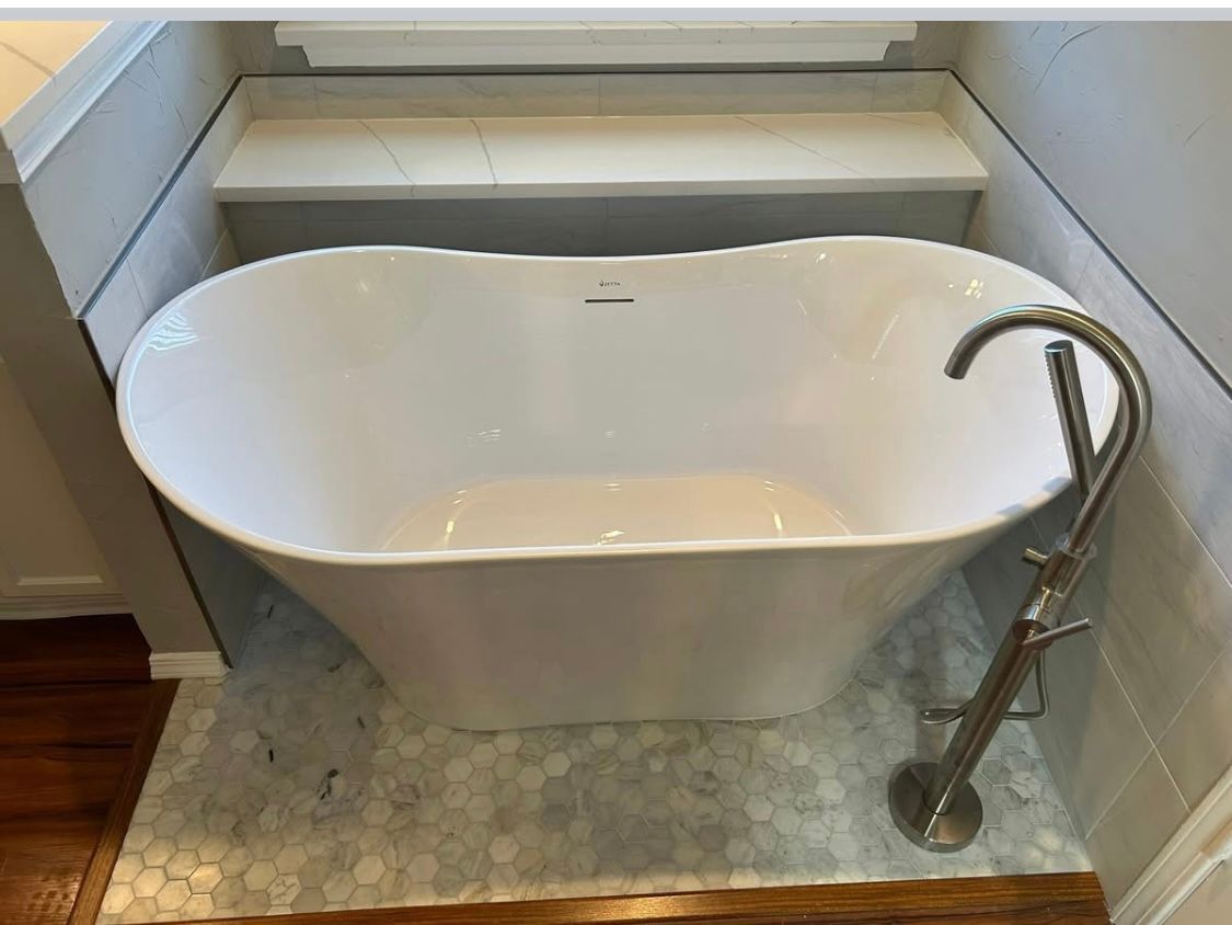 A white, freestanding bathtub in a bathroom with a marble tile floor and a brushed nickel faucet.