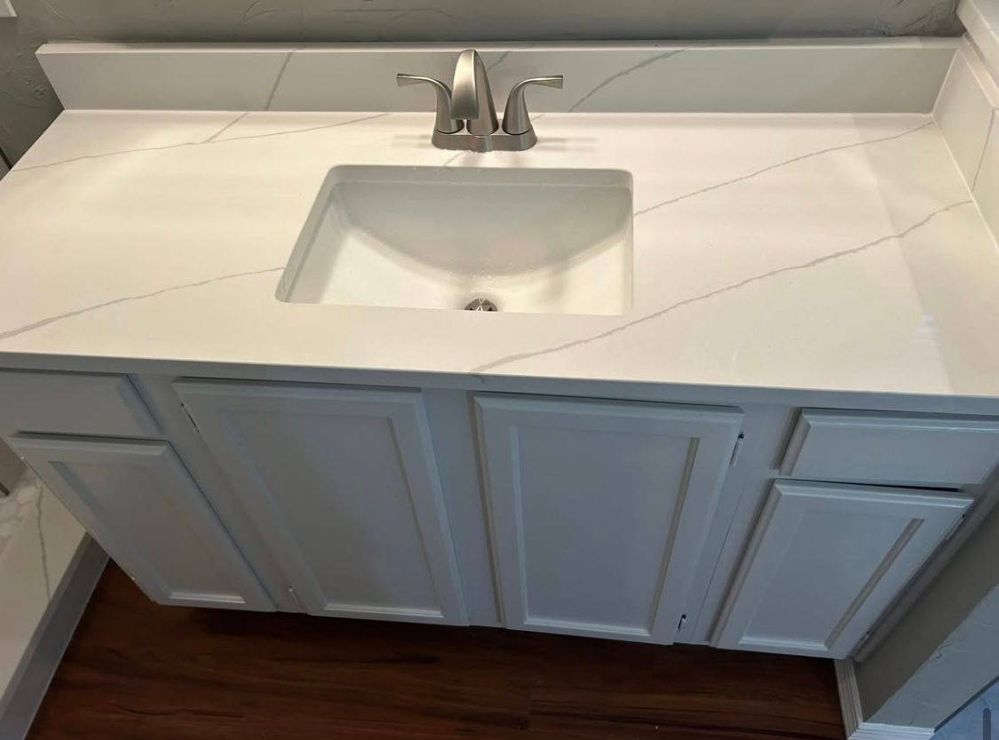 White bathroom vanity with marble countertop and sink, set against a wall. Cabinet doors are white, with a silver faucet.