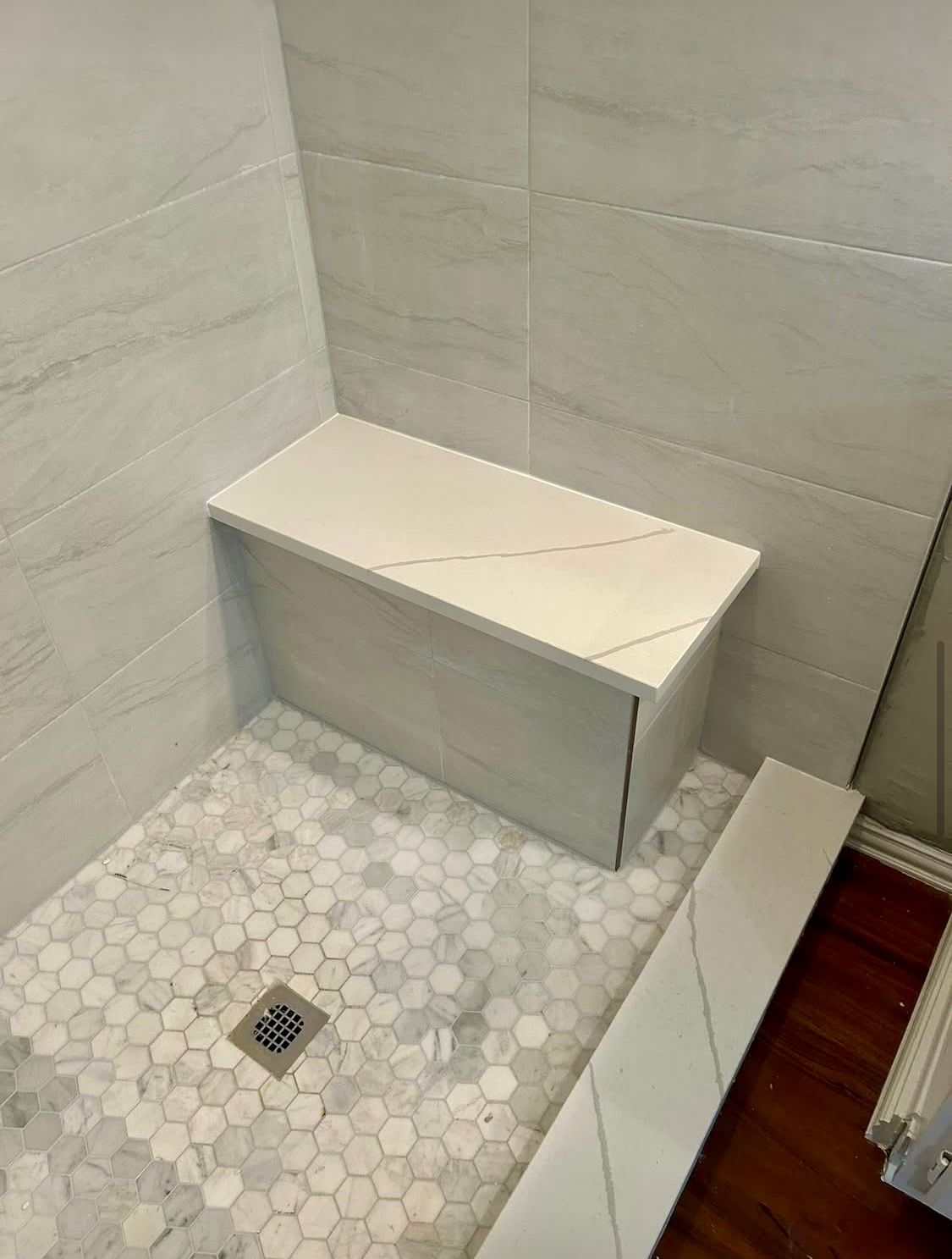 Shower with white tiled walls, a built-in bench, and a hexagonal mosaic tile floor.