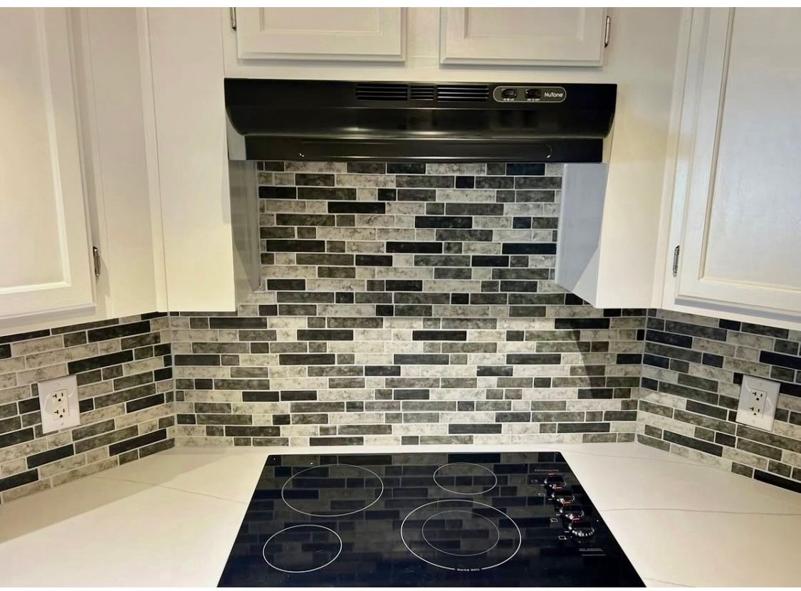 Kitchen backsplash with mosaic tile above a black stovetop. White cabinets flank the stove.