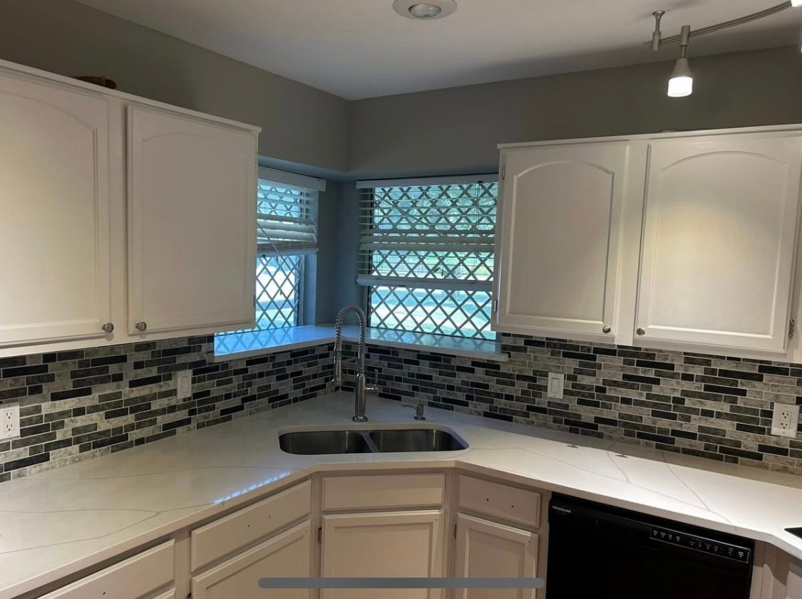 Kitchen with white cabinets, gray backsplash, and a stainless steel sink.