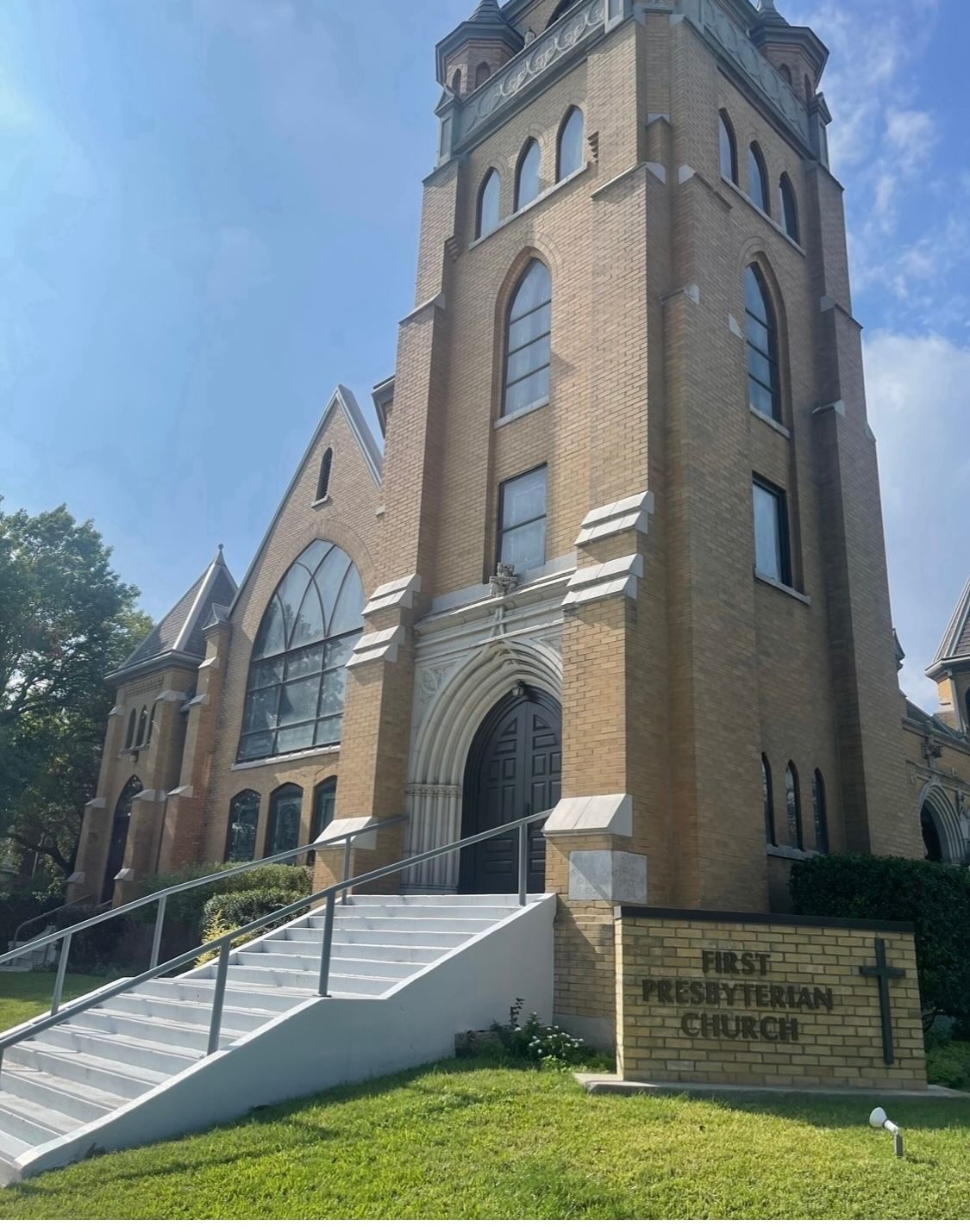 First Presbyterian Church building with tower and arched doorway. Sign in front.