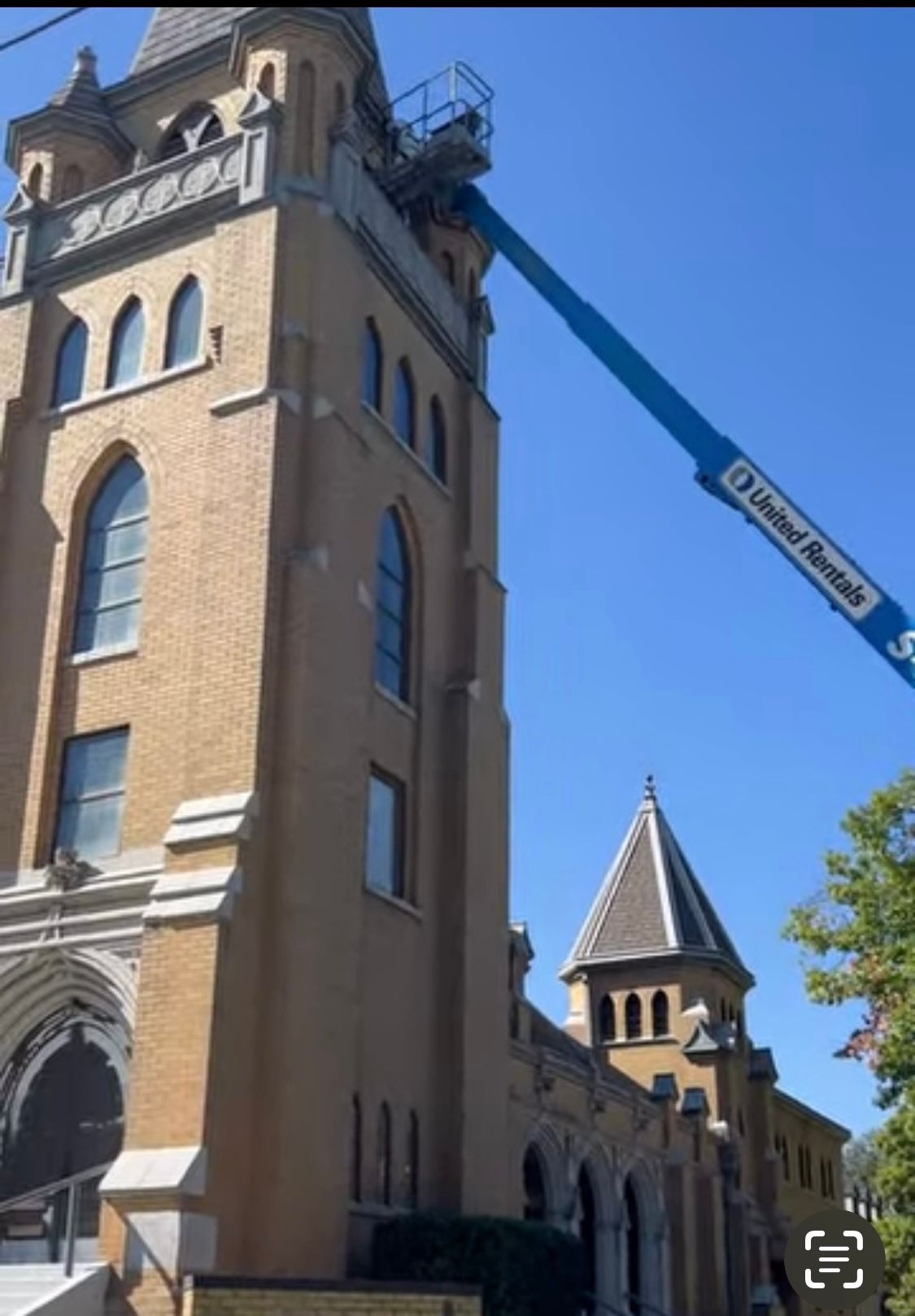 A tall brick church with arched windows; a blue lift platform at the top.