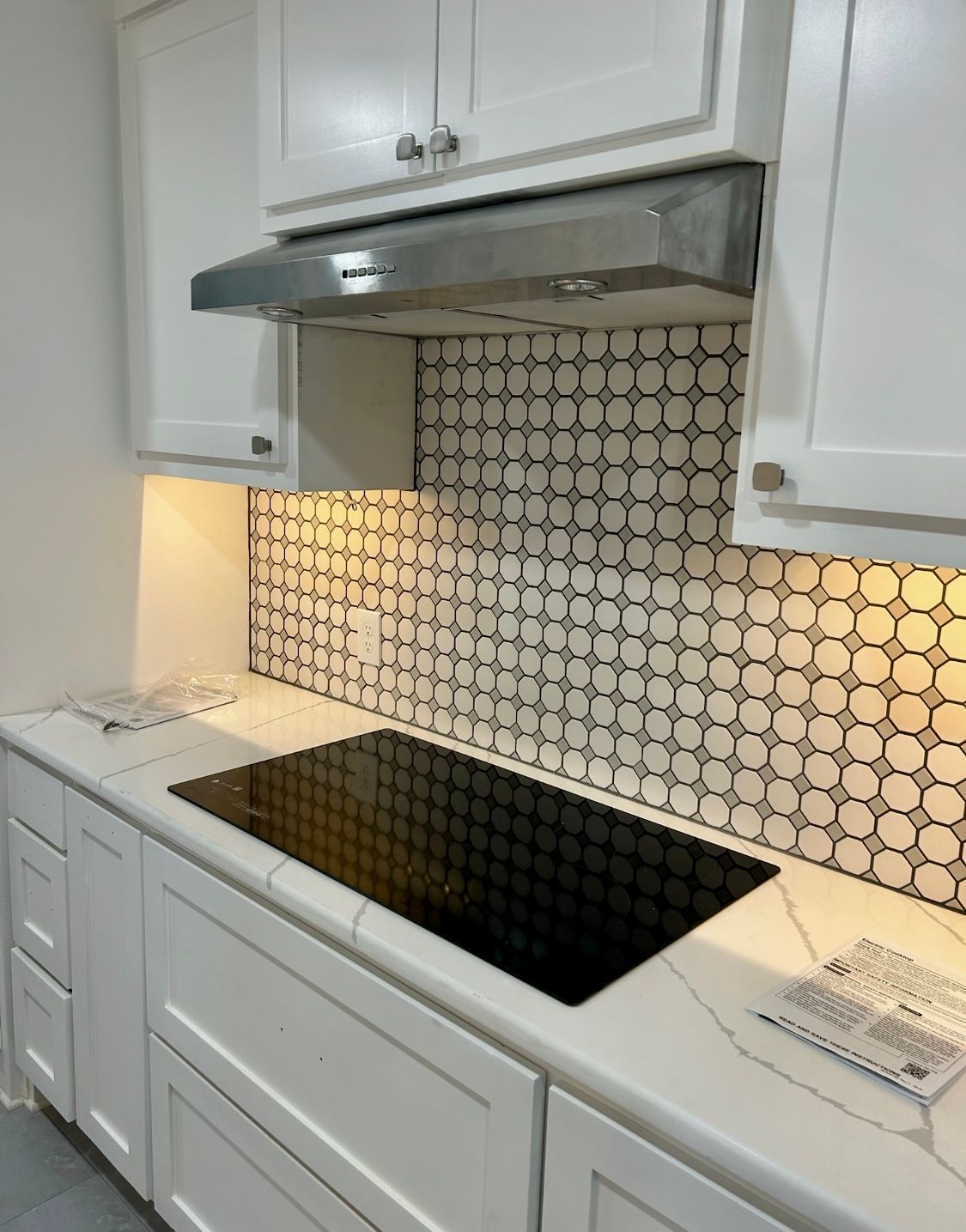 White kitchen with a black stovetop, white cabinets, and patterned backsplash.