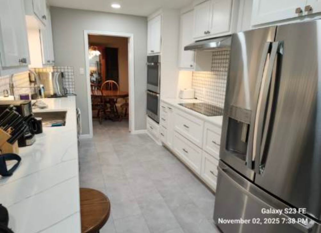 White kitchen with stainless steel appliances, white cabinets, gray countertops, and tile flooring.
