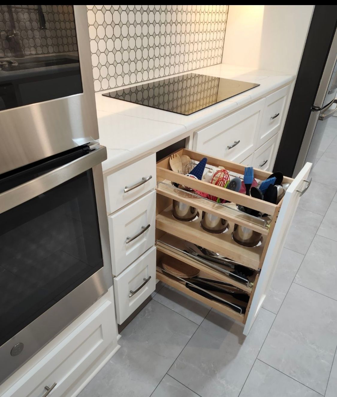 Kitchen cabinet with pull-out storage for utensils and cookware, next to a stove and oven.
